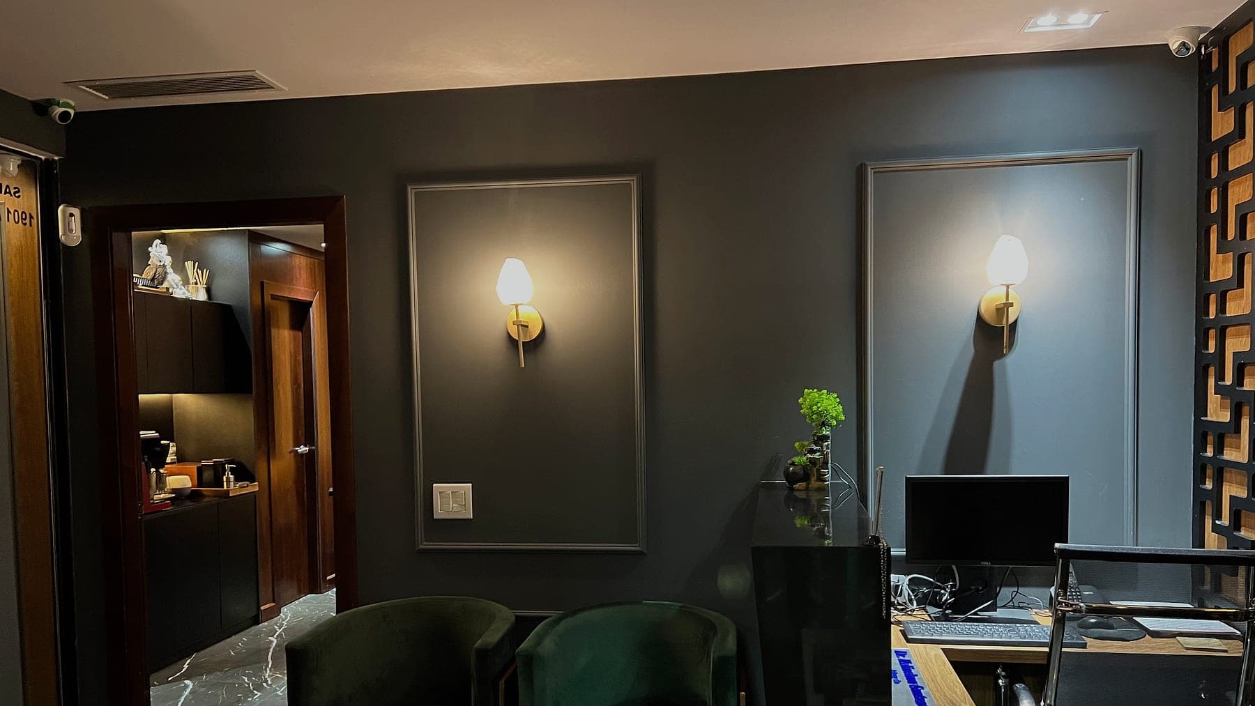 Sala de espera do escritório, com poltronas verdes e arandelas de latão