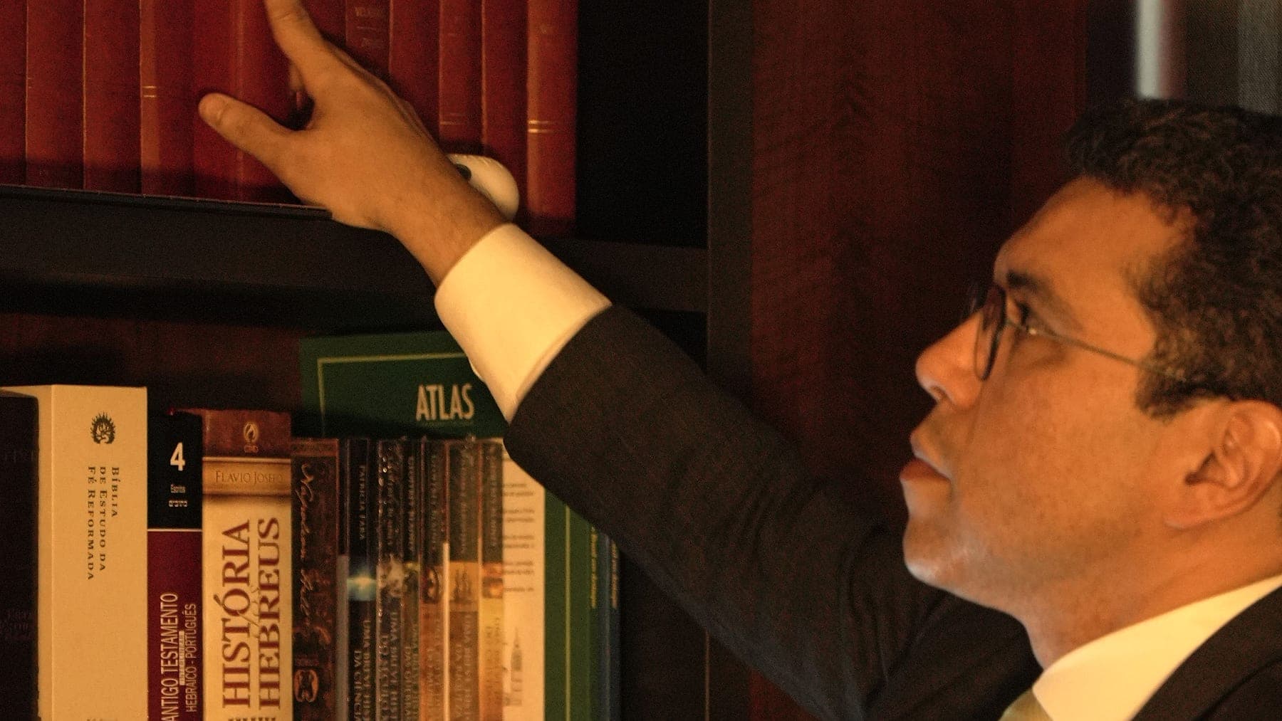 Dr. Helinelson Lombardo Santana alcançando um volume na estante do escritório
